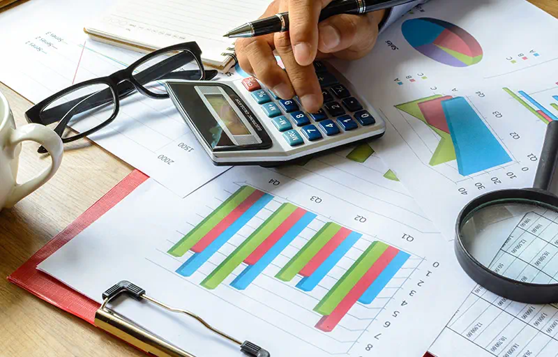 Papers with charts and graphs with a hand resting over a calculator.