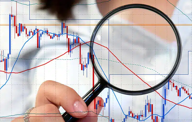 A bar and line graph close up with a woman holding a magnifying glass up to it.
