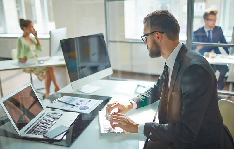 A business man looks at his laptop while typing in a modern office.