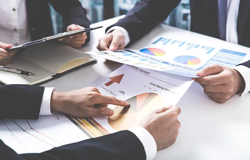 Market Analysis & Advisory Three business people reviewing reports with charts and graphs.